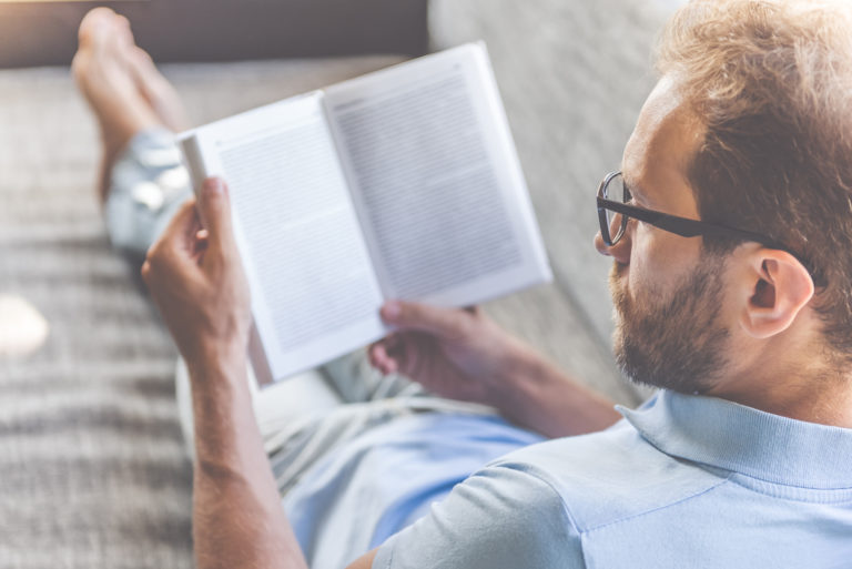 Hombre descalzo y relajado recostado sobre un sillón, leyendo.