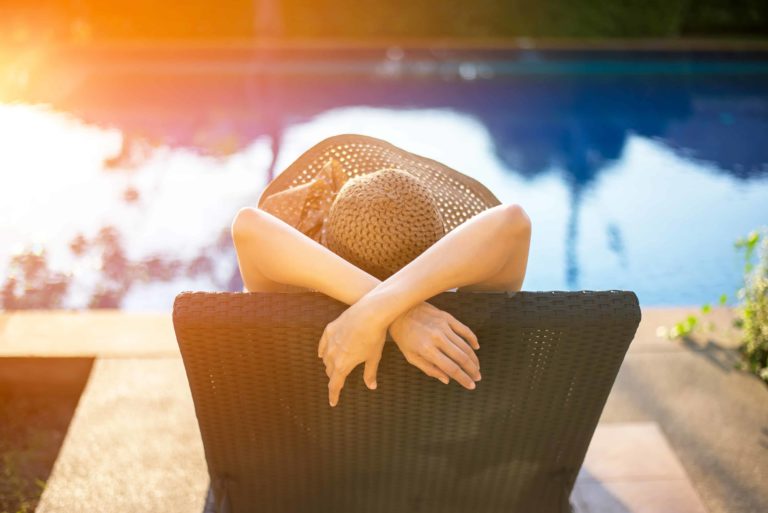 mujer con sombrero disfrutando del sol al lado de una piscina