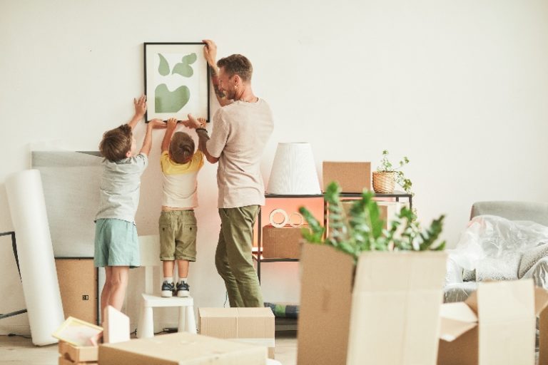 Un papá y dos hijos colocan un cuadro en la pared